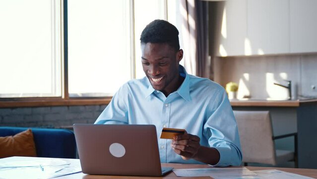 Concentrated financial director in a shirt looks at bank card in hand and enters digits to laptop