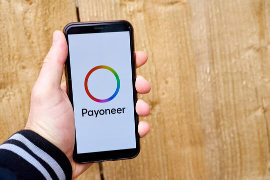 Ukraine, Kyiv, May 3, 2022 - Hand holding smartphone with payoneer logo on wooden background. payoneer logo.