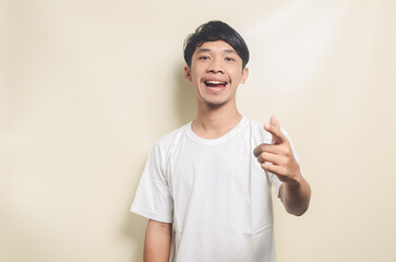asian man wearing white t-shirt happy while pointing his hand forward isolated background