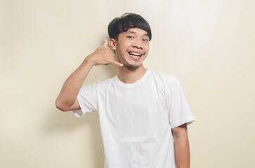 asian man wearing white t-shirt with phone gesture with his hands on isolated background