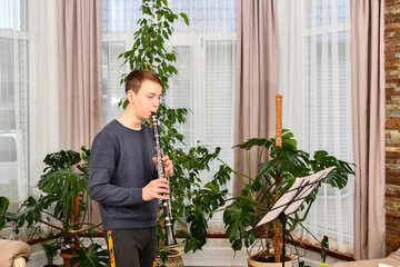 The teenager diligently plays the clarinet. Learning music at home. - obrazy, fototapety, plakaty