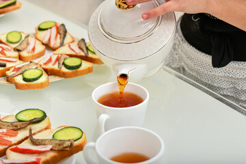 A girl pours tea leaves from a teapot into a cup for drinking tea with sandwiches.