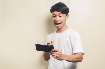 Naklejka premium asian man wearing white t-shirt with surprised gesture after getting a message by phone on isolated background