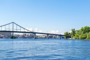 Scenic nature travel cityscape river Dnipro with blue water and metal pedestrian bridge at sunny summer day in Kiev. View from inside river, ship on water