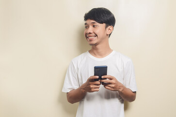 asian man wearing white t-shirt carrying phone and looking at empty space on isolated background
