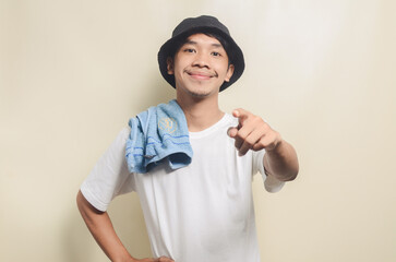 happy asian man wearing bright white t-shirt with black hat and holding towel gesturing his hand on isolated background