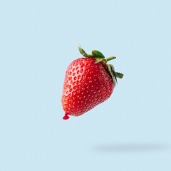 Flying or levitate balloon made of strawberry on pastel blue background. Minimalistic summer fruit layout. Creative food concept.