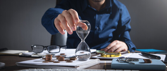 Businessman holding hourglass. Coins and business objects on the desk