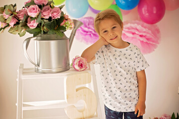 Cute child, preschool boy, celebrating birthday at home, holding number five wooden number, balloons and decoration