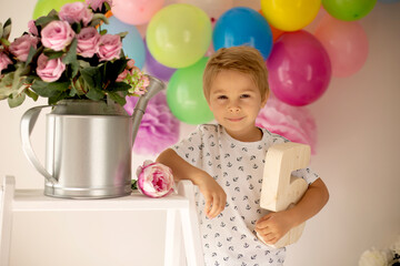 Cute child, preschool boy, celebrating birthday at home, holding number five wooden number, balloons and decoration