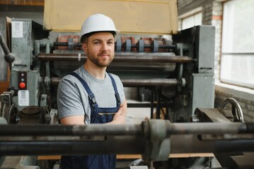 Smiling and happy employee. Industrial worker indoors in factory. Young technician with white hard hat.