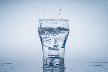 Ice cube fell into the glass of water. Water splashed from the clear glass. Fresh concept