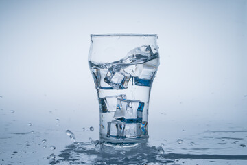 Ice cube fell into the glass of water. Water splashed from the clear glass. Fresh concept