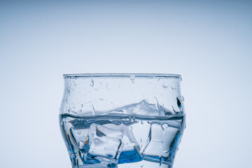 Ice cube fell into the glass of water. Water splashed from the clear glass. Fresh concept