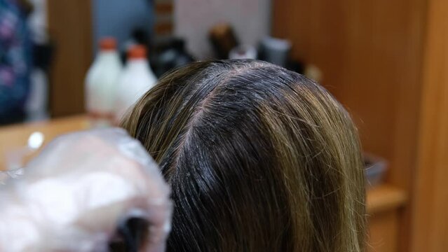 Hair coloring close-up. Hairdresser paints brunette hair roots with brush. Slow motion
