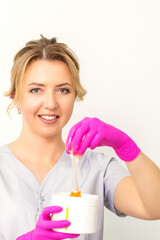 Obraz na płótnie Canvas Portrait of a female caucasian beautician holding a jar of sugar paste for sugaring wearing pink gloves on white background