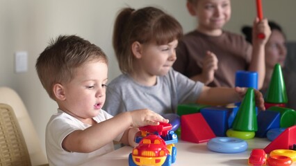 little boy and baby girl play in kindergarten. a group of children play toys cubes and cars on the table in kindergarten. happy family preschool education concept. nursery indoor baby toddler home