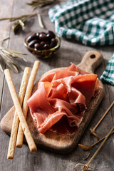 Spanish serrano ham with olives and breadstick on wooden table background	