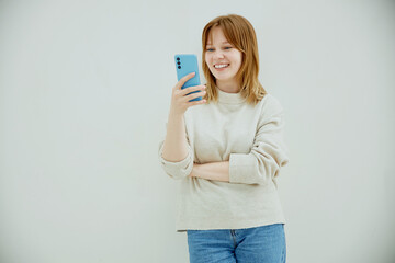 Young cute caucasian woman using smartphone while standing against white wall