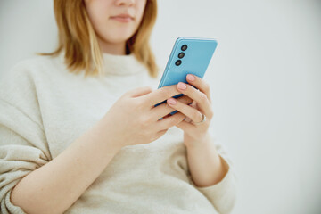 young blonde girl using smartphone close-up against white wall