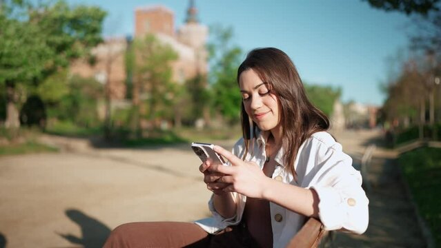 Pretty brunette woman typing on mobile while sitting on the bench