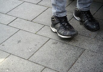 Schwarzes Paar Lederschuhe mit grauen Jeanshosenbeinen auf grauem Steinplatten in Stadt 