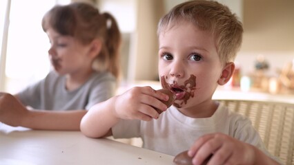 children eat chocolate. dirty little baby kids in the kitchen eating chocolate in the morning. happy family eating sweets kid dream concept. baby dirty face lifestyle eating chocolate cocoa