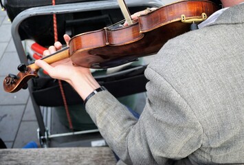 Oberkörper von jungem Mann im beige-grauen Blazer sitzt auf Bank im Freien und spielt Geige 