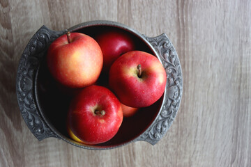 Silver bowl full of red apples on wooden table. Top view.