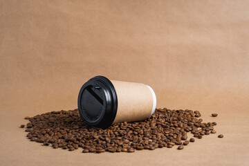 Takeaway brown paper coffee cup with black cap lie on roasted beans at brown background. Mock up