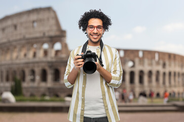 travel, tourism and photography concept - happy smiling man or photographer in glasses with digital camera over coliseum in rome, italy on background