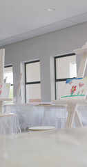 Vertical image of empty white painting classroom with painting equipment and easel