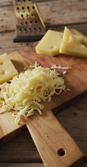 Vertical image of grated cheese and pieces of cheese with grater on wooden board