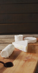 Vertical image of few types of fresh cheese on wooden chopping board and rustic background