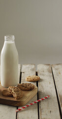 Vertical image of chocolate chip cookies and bottle of milk on chopping board and wooden background