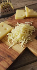 Foto op Plexiglas Vertical image of grated cheese and pieces of cheese with grater on wooden board © vectorfusionart