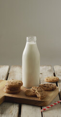 Vertical image of chocolate chip cookies and bottle of milk on chopping board and wooden background