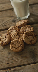 Vertical image of chocolate chip cookies and glass of milk on wooden background