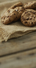 Vertical image of chocolate chip cookies on cloth and wooden background