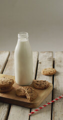 Vertical image of chocolate chip cookies and glass of milk on chopping board and wooden background