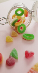 Vertical image of jelly candy spilling out of glass jar on pink background