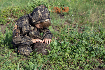 small boy looks curiously at hedgehog caught in forest. Child with pet.