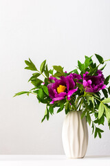 Paeonia suffruticosa in a white vase against a white wall, part of a home interior, house decoration with flowers Japanese Tree Peony, cozy spring May background