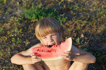 Six years old boy eating watermelon in garden sitting on ground