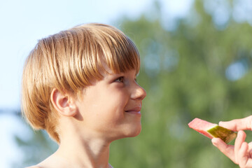 Boy smiling looks at person who gives him piece of watermelon
