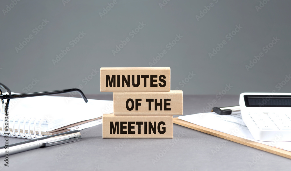 Poster minutes of the meeting text on wooden block with notebook,chart and calculator, grey background