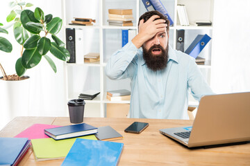 Frustated man clutching head working at laptop in office, frustration
