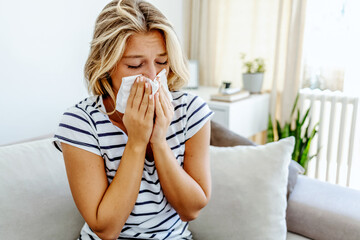 Shot of an attractive young woman feeling ill and blowing her nose with a tissue at home. Photo of...