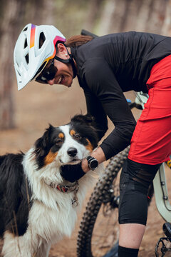 Girl with helmet and enduro mtb bike petting her australian shepherd dog in the mountains