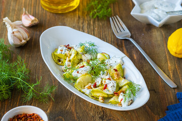 Healthy food, grilled zucchini salad with yogurt sauce, herbs, walnuts in a gray oval plate on a wooden background. Turkish cuisine.